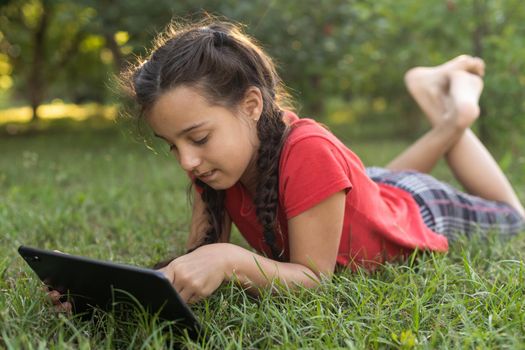 Child girl playing on a Digital tablet in the garden. Online or Remote education concept.