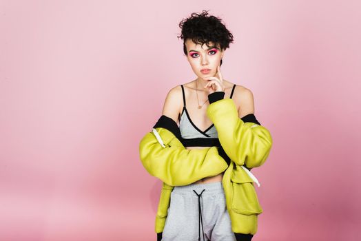 Beautiful teenager girl sincerely smiles and laughs in sports stylish clothes in the studio on a pink background.