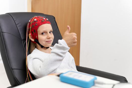 Girl receiving biofeedback therapy sitting on a chair and gesturing to be well with thumbs up
