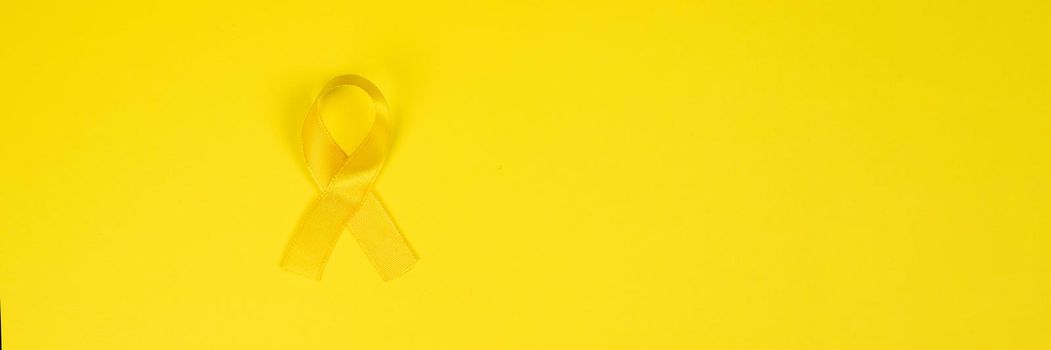 Yellow gold ribbon on a yellow background. Children cancer concept. Awareness month. Childhood Cancer Day February, 15. Web banner.