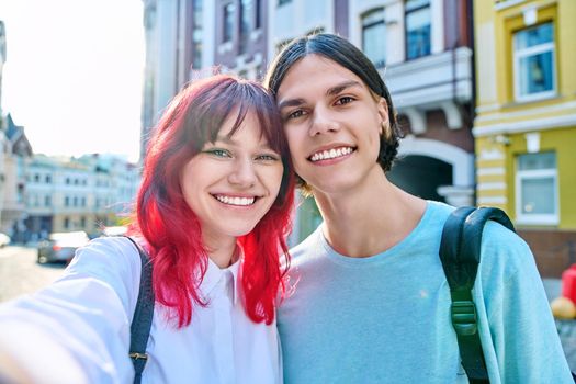 Young teenage friends guy and girl having fun, laughing, taking selfie photo. Youth couple enjoy vacation, weekend, holiday, city street background. Fun, joy, happiness concept
