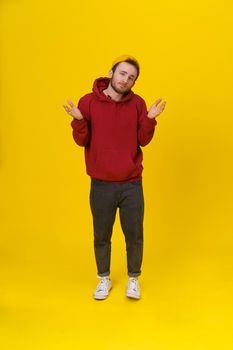 Gesturing with both hands I DONT KNOW handsome young man in casual wear, with hands lifted up looking at camera on yellow background. Hipster fashion bearded smart man casual look.