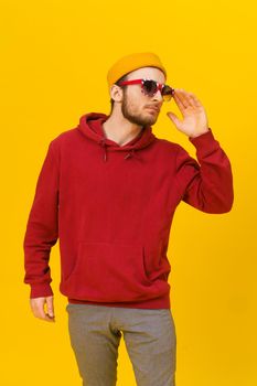 Young pensive handsome caucasian man in Great Britain flag sunglasses and casual wear, looking away isolated on yellow background. Stylish bearded smart hipster man casual look.