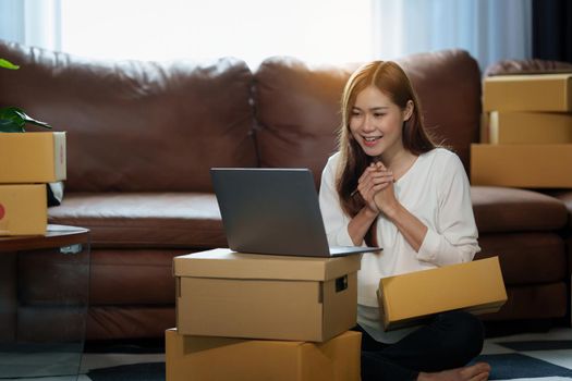 Image of Young asian woman startup freelance with parcel box and talking with customer by computer laptop. Online marketing packing box delivery concept