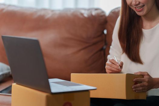 Image of Young asian woman startup freelance with parcel box and talking with customer by computer laptop. Online marketing packing box delivery concept