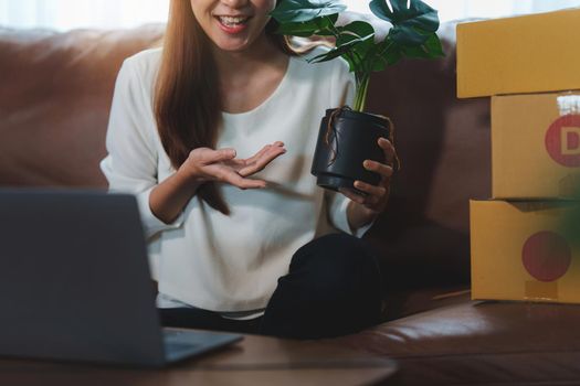 Image of Young asian woman startup freelance with flower and showing to customer by computer laptop. Online marketing packing box delivery concept