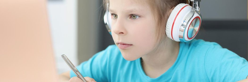 A girl in headphones looks attentively into a laptop, close-up. Distance learning during a pandemic, completing school assignments