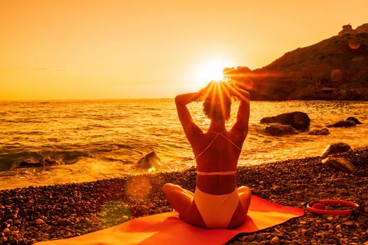 Young woman in swimsuit with long hair practicing stretching outdoors on yoga mat by the sea on a sunny day. Women's yoga fitness pilates routine. Healthy lifestyle, harmony and meditation concept.