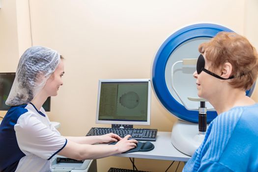 A girl optometrist examines the eyes of a patient using special modern equipment.