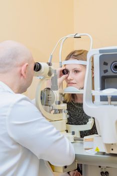 A male ophthalmologist checks the eyesight of a young girl using a modern device with a light beam.