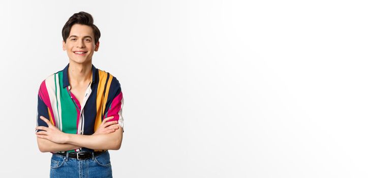 Hansome smiling gay man looking happy, standing over white background in summer outfit.