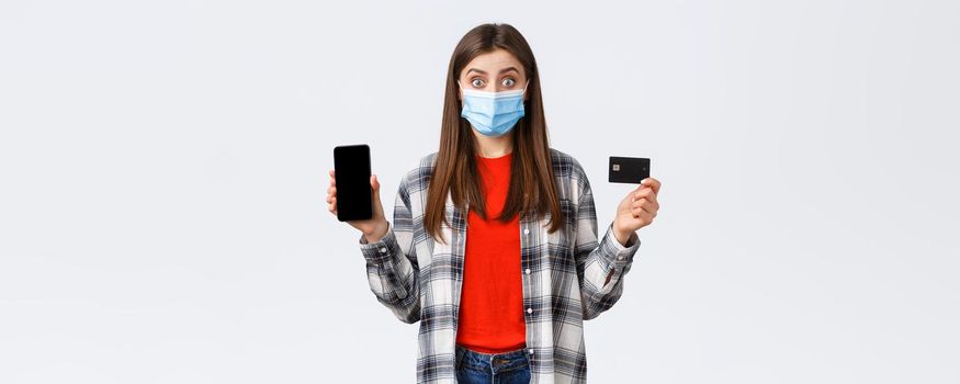 Coronavirus outbreak, working from home, online shopping and contactless payment concept. Excited woman in medical mask showing credit card and mobile phone, look surprised.
