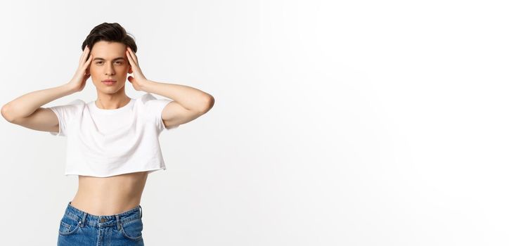Lgbtq and pride concept. Beautiful and confident gay man wearing crop top, touching face and looking sassy at camera, standing over white background.