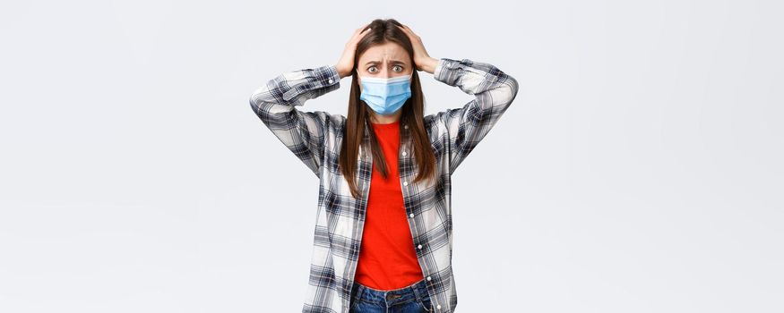 Different emotions, covid-19 pandemic, coronavirus self-quarantine and social distancing concept. Alarmed and worried, panicking young woman in medical mask, grab head indecisive, feel scared.
