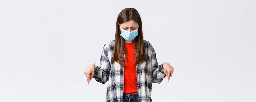 Coronavirus outbreak, leisure on quarantine, social distancing and emotions concept. Confused and unsure young woman in medical mask stare puzzled at something down, point bottom promo.