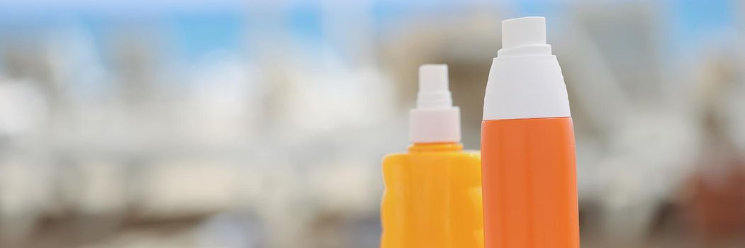 Orange plastic bottles and a beige towel on a beach lounger, close-up, blurry. Cosmetics for sunbathing and relaxation at sea