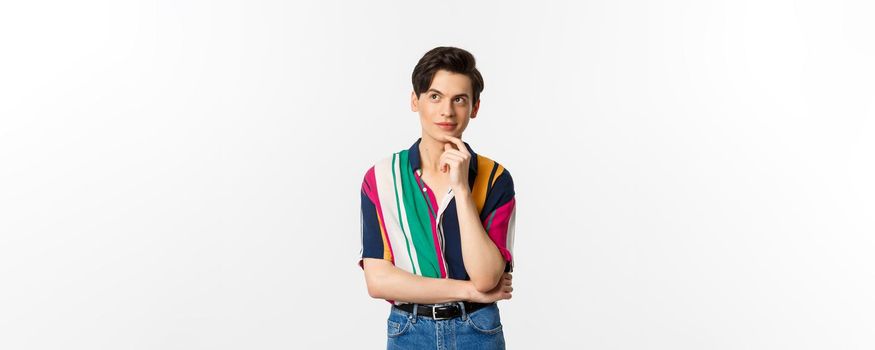 Creative young man thinking and smiling, looking at upper left corner thoughtful, standing over white background.