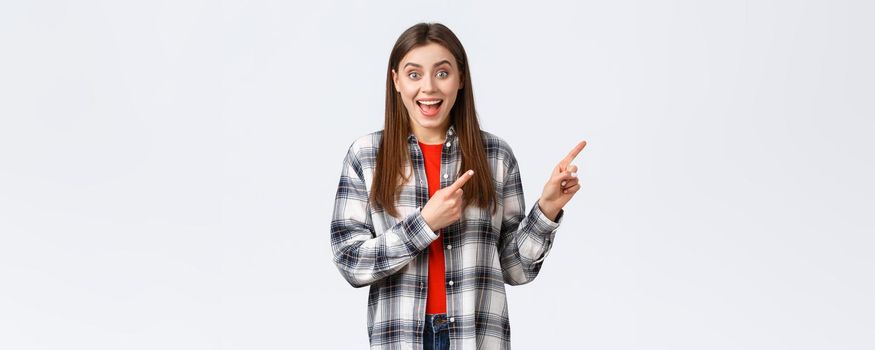 Lifestyle, different emotions, leisure activities concept. Excited girl in checked casual shirt gladly tell about great dicounts, pointing fingers upper right corner, talking to you, rejoicing.