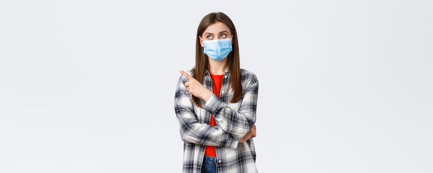Coronavirus outbreak, leisure on quarantine, social distancing and emotions concept. Young pretty girl in medical mask staying home, search job freelance, pointing finger upper left corner pleased.