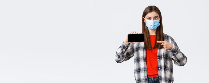 Different emotions, covid-19, social distancing and technology concept. Attractive woman in medical mask advice download this, point finger at mobile phone screen, recommend application or game.