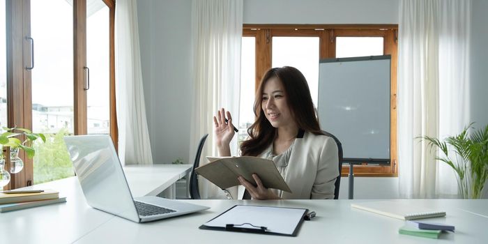 Asian female talking about sale report in video conference. Asian team using laptop and tablet online meeting in video call.Working from home remotely..