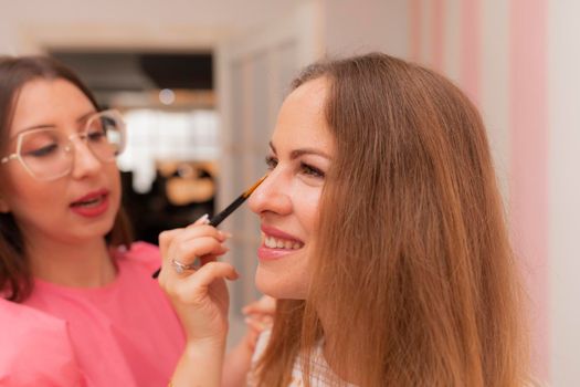 A beautician applying makeup on her client's face while she smiles during a session at the beauty salon