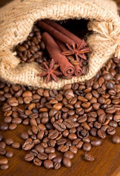 Coffee beans, two cinnamon sticks, a piece of chocolate and two anise stars are scattered on a wooden table. Copy space.