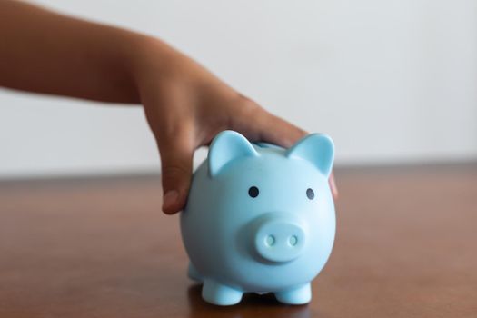 Child's hand is holding a piggy bank on wooden table. Saving money concept for the future. Planning for support