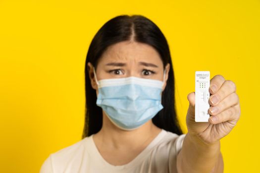 Showing positive test scared of pandemic mature asian woman wearing medical face mask coronavirus or monkeypox prevention. Middle age woman in white t-shirt and medical mask on yellow background.