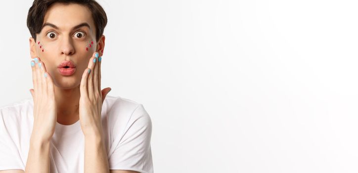 People, lgbtq and beauty concept. Close-up of handsome gay man express surprise, showing hands with blue nail polish, standing over white background.