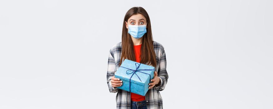 Covid-19, lifestyle, holidays and celebration concept. Excited cute birthday girl holding wrapped box, curious what inside, receive gift, wearing medical mask to prevent coronavirus outbreak.