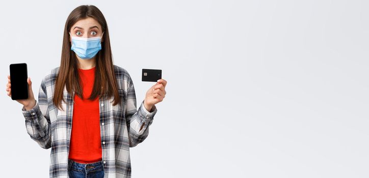 Coronavirus outbreak, working from home, online shopping and contactless payment concept. Excited woman in medical mask showing credit card and mobile phone, look surprised.