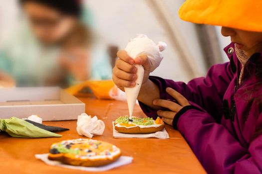 Little girl decorates cookies for Halloween. Children's art project, a craft for children