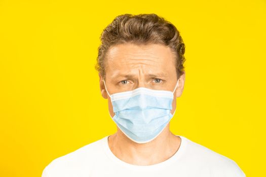 Sad handsome man wearing medical face mask prevention pandemic coronavirus or monkeypox. Handsome man in white t-shirt and medical mask on yellow background. Panoramic, healthcare concept.