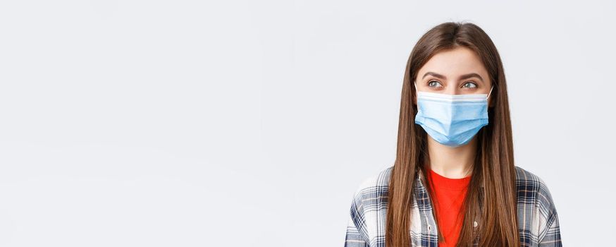 Coronavirus outbreak, leisure on quarantine, social distancing and emotions concept. Close-up of pleased cute girl smiling in medical mask, looking left at pleasant good thing, white background.