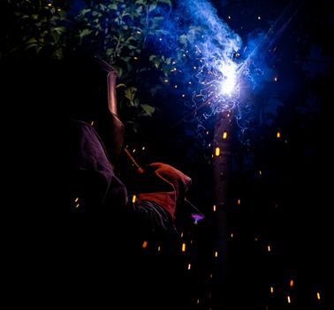 Worker with protective mask welding metal and producing smoke and sparks. arc welding. welder working welding steel