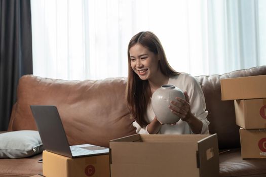 A female entrepreneur selling ceramic jar via live streaming laptop computer and checking orders from customer for online shopping concept.