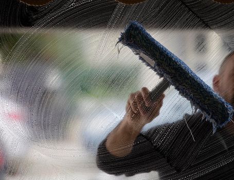 An employee of a professional cleaning service in overalls washes the glass of the windows of the facade of the building. Showcase cleaning for shops and businesses. High quality photo