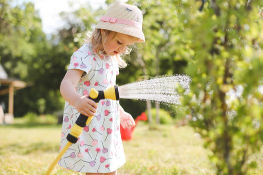 Adorable little girl playing with a garden hose on hot sunny summer day