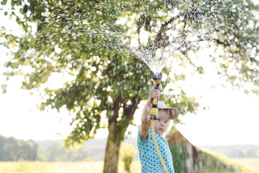 Adorable little girl playing with a garden hose on hot sunny summer day