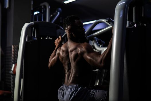 Shirtless african american man doing back exercises on a machine in the gym