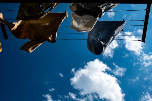 clothes are dried on the wind on background blue sky with clouds. T-shirts hanging on a clothesline