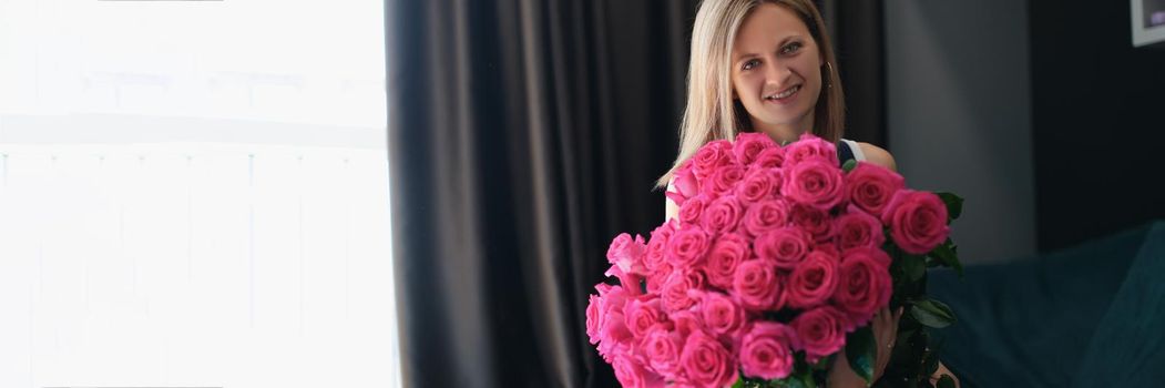 A young woman is sitting on a sofa with a large bouquet of roses, close-up. Romance, holiday greetings, wedding anniversary