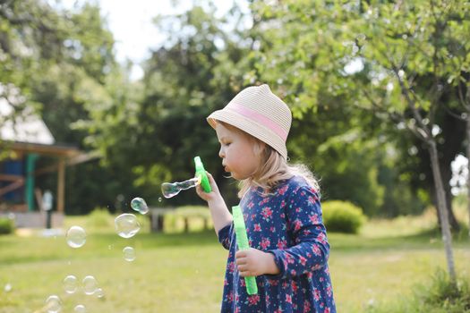 Cute little girl blowing soap bubbles on a walk in summer outdoors.