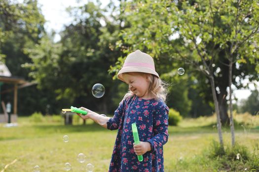 Cute little girl blowing soap bubbles on a walk in summer outdoors.