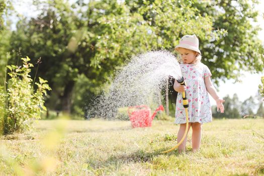 Adorable little girl playing with a garden hose on hot sunny summer day