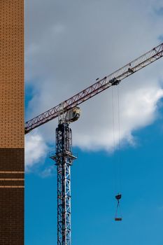 Building crane lifts building materials. Construction, building a house. Construction crane with blue sky and clouds. Vertical.