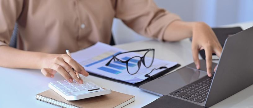 Cropped image of female accountant working with laptop computer and using calculator.