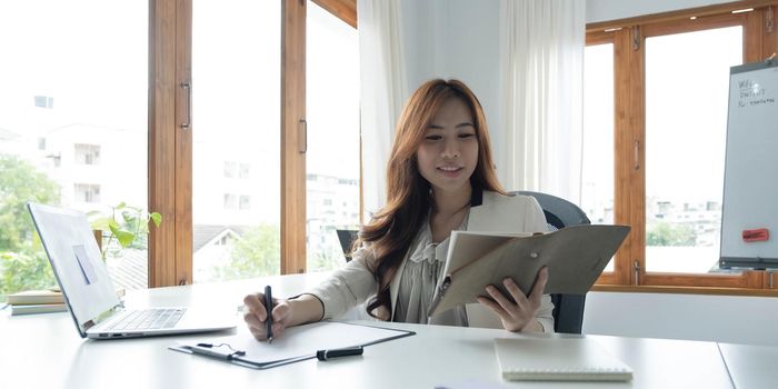 Portrait of an Asian young business Female working on a laptop computer in her workstation.Business people employee freelance online report marketing e-commerce telemarketing concept..