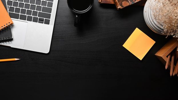 Modern workplace with laptop computer, coffee cup and supplies on black table.